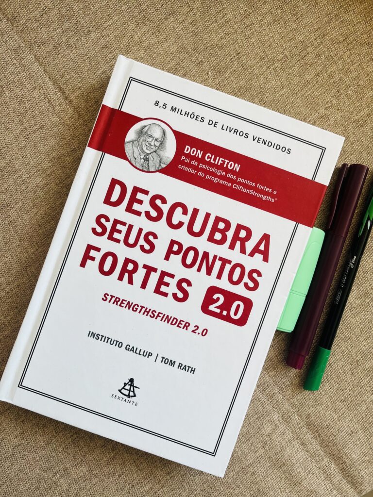  foto do livro ''descubra seus pontos fortes'' ao lado dele, algumas canetas. 